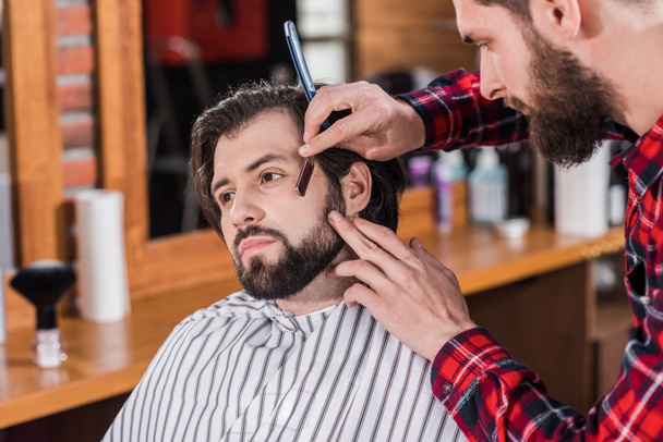 jeune coiffeur en chemise à carreaux rasage homme avec machine à couper les cheveux
 - Photo, image
