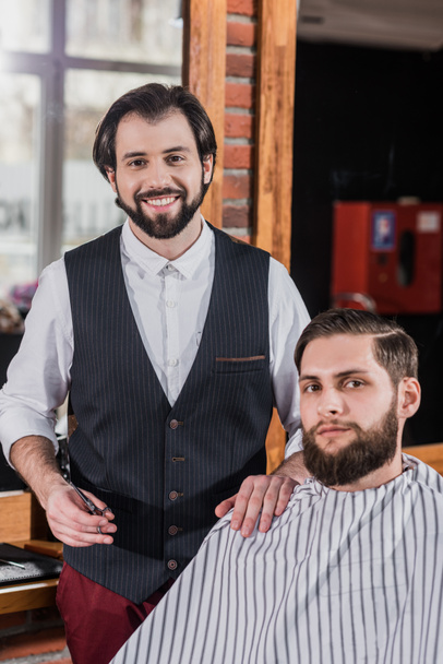 smiling bearded barber with client at barbershop - Foto, Imagen