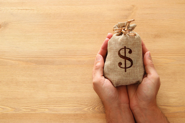 Male hand holding a sack of money over wooden desk - Photo, image