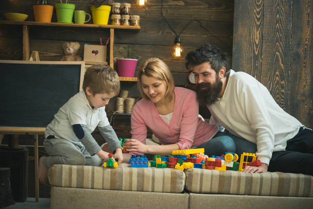 Kid with parents play with plastic blocks, build construction. Caring parents concept. Family on busy face spend time together in playroom. Father, mother and cute son play with constructor bricks. - Foto, Imagem