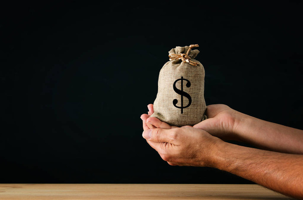 Male hand holding a sack of money over wooden desk - Φωτογραφία, εικόνα