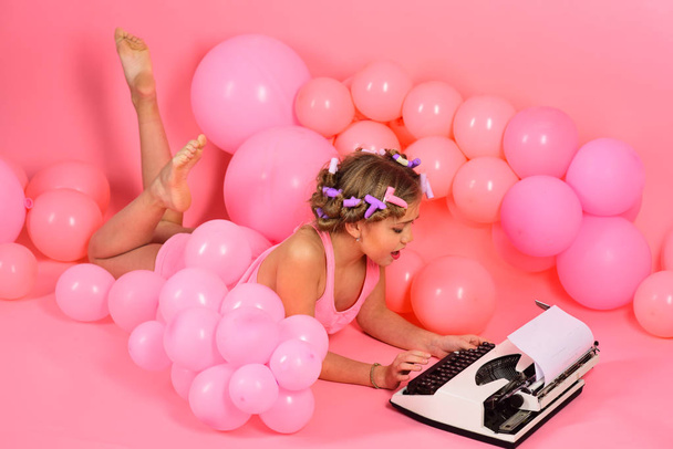 Education and childhood. Child in underwear with typewriter on pink background. Kid journalist or writer, career. Little girl secretary at party balloons. Small girl with curler in hair typing. - Fotó, kép