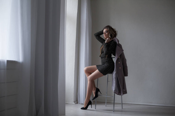 girl with gray coat sits on a Chair looking out of the window - Foto, Imagen