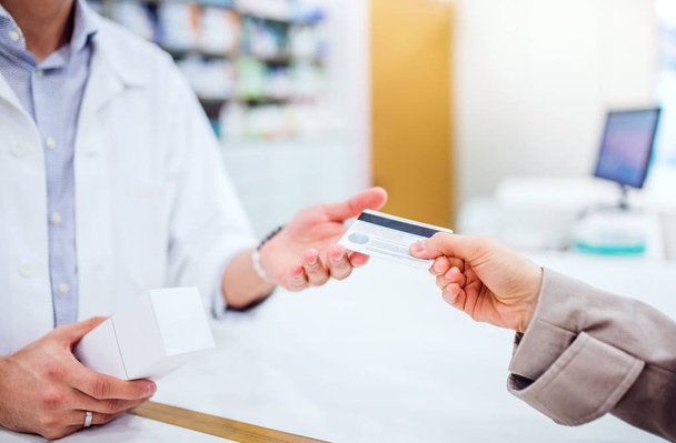 Unrecognizable customer giving a credit card to a male pharmacist. - Foto, afbeelding