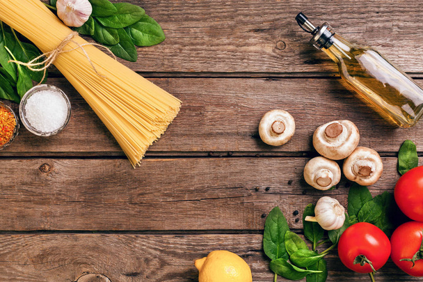 De ingrediënten van pasta - tomaten, olijfolie, knoflook, Italiaanse kruiden, verse basilicum, zout en spaghetti op een houten achtergrond met kopie ruimte, horizontale, top uitzicht. Stilleven. Flay lay - Foto, afbeelding