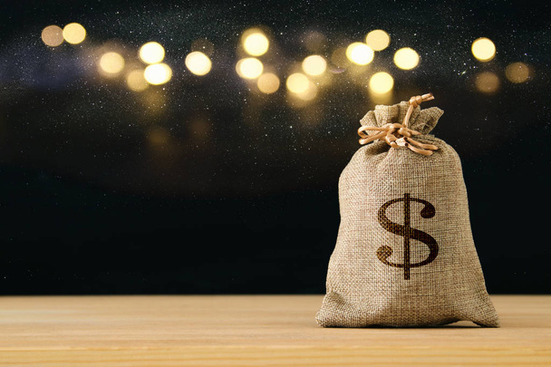 A sack of money over wooden desk and glitter black background. - Photo, image