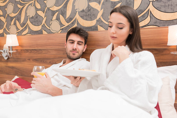Attractive young couple in white robes, enjoying food and drink  - Foto, Imagem
