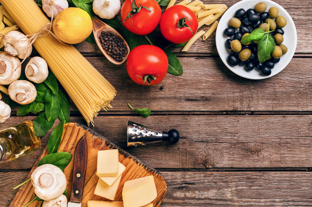Итальянская кухня-помидоры, базилик, макароны, оливковое масло и сыр на деревянном фоне, вид сверху, копировальное пространство
. - Фото, изображение