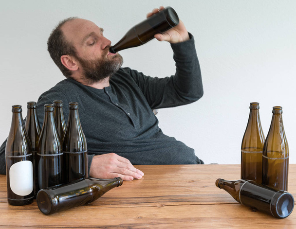 középkorú alkoholos ember, sok sör üveg ül egy fa asztal - Fotó, kép