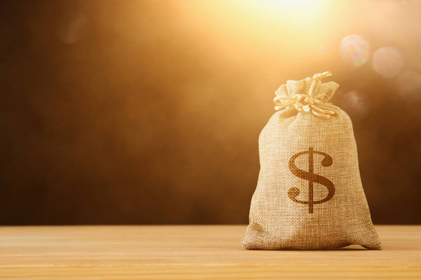 A sack of money over wooden desk and glitter black background. - Фото, изображение