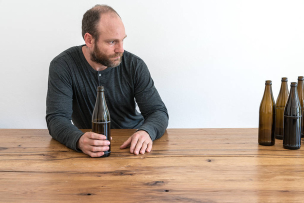 αλκοολούχα μεσήλικα με μια γενειάδα και πολλά μπουκάλια άδειο μπύρα σε ένα τραπέζι μπροστά του - Φωτογραφία, εικόνα
