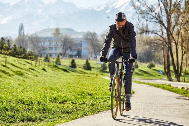 Un ciclista cavalca su una strada in città su uno sfondo di erba verde e montagne
. - Foto, immagini