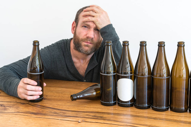 uomo alcolizzato di mezza età con la barba e molte bottiglie di birra vuote su un tavolo davanti a lui
 - Foto, immagini