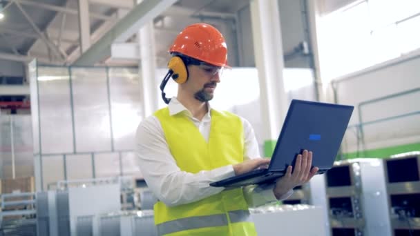 Een mens in harde hoed op zijn laptop werken in een industriële fabriek. - Video