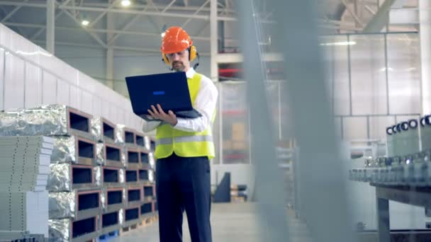 Mannelijke werknemer typen op zijn laptop, permanent in een magazijn, fabrieksinstallaties. - Video