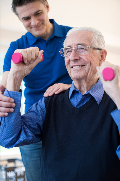 Physiotherapist Helping Senior Man To Lift Hand Weights - Foto, immagini