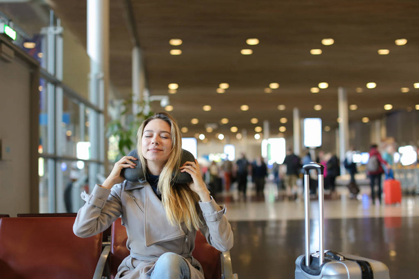 Mujer sentada con almohada y equipaje en la sala de espera del aeropuerto
. - Foto, Imagen