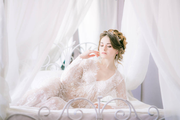 Portrait of beautiful bride. Morning of the bride. Wedding morning. Makeup. Bride with cones and fair hair. Fragile bride in white lace negligee - Foto, Bild