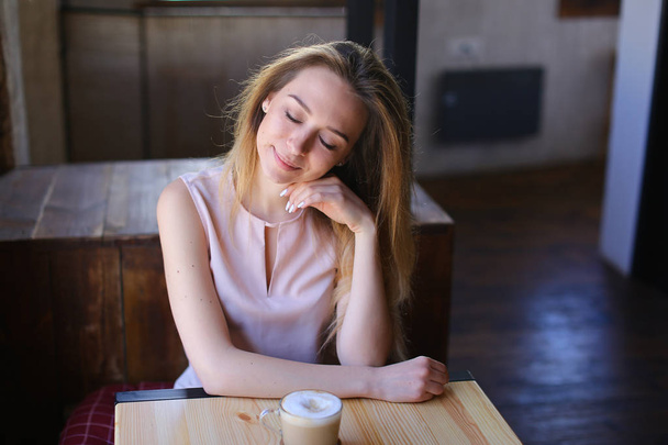 Menina satisfeita sentada perto da mesa de madeira com xícara de cappuccino no café e relaxante
. - Foto, Imagem