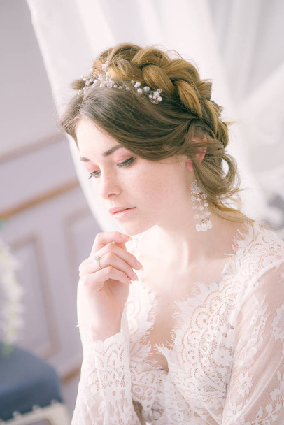 Portrait of beautiful bride. Morning of the bride. Wedding morning. Makeup. Bride with cones and fair hair. Fragile bride in white lace negligee - Foto, Imagem