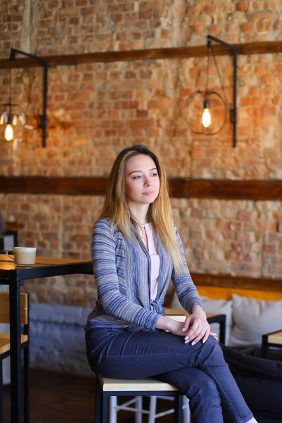 Ικανοποιημένοι κορίτσι που κάθεται κοντά σε πίνακα στο φιλόξενο café με ασυνήθιστη εσωτερικό. - Φωτογραφία, εικόνα
