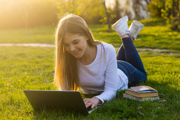 Jeune belle étudiante avec un ordinateur portable se trouve sur l'herbe dans
 - Photo, image