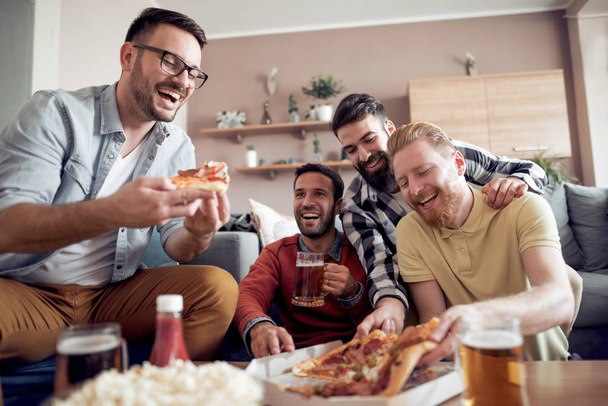 Четверо друзей смотрят телевизор дома, едят пиццу и пьют пиво.
. - Фото, изображение