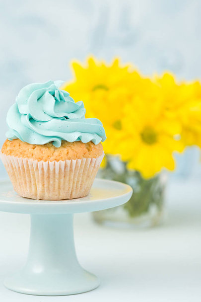Cupcake with blue cream decoration on vintage stand and bouquet of yellow chrysanthemum in glasses vase. - Foto, immagini