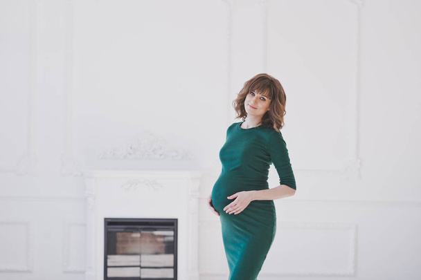A pregnant girl in a green dress stands among the room 1114. - Foto, immagini