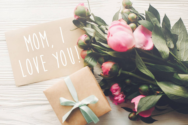 mom i love you text on craft card and pink peonies bouquet with gift box on rustic white wooden background in light.  - Photo, Image