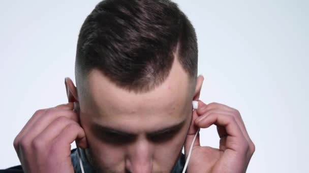portrait of young handsome man in headphones listening to music on his phone isolated on a white background - Materiał filmowy, wideo