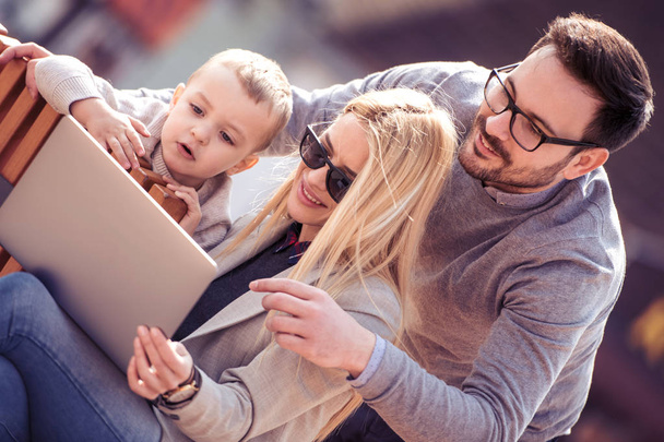 Onnellinen nuori perhe hauskaa ulkona kannettavan tietokoneen kanssa
. - Valokuva, kuva