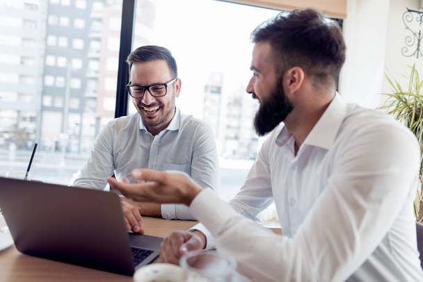 Dois empresários confiantes com um sorriso verificam o trabalho no laptop no escritório
. - Foto, Imagem