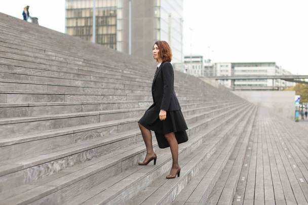 Businesswoman going up on stairs in high buildings background. - Photo, Image