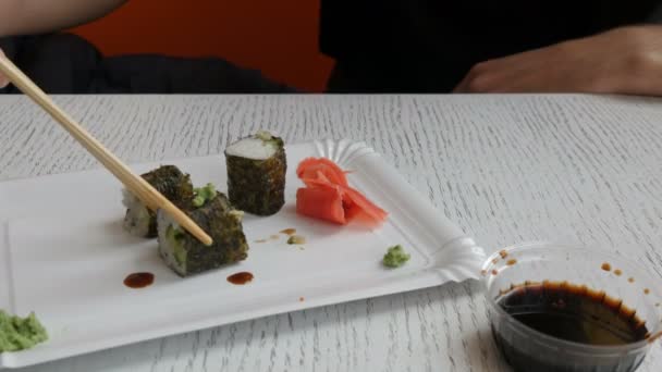 Mann nimmt eine chinesische Bambusstäbchen-Sushi-Rolle und taucht sie in Sojasauce - Filmmaterial, Video