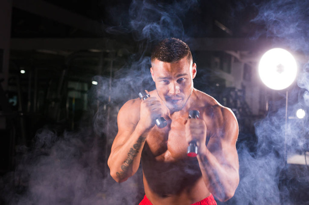 Могущественный человек делает упражнения по боксу, делая прямой удар гантелями. Фото спортивного мускулистого мужчины. Сила и мотивация
 - Фото, изображение
