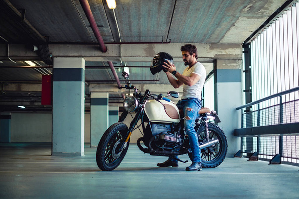 Человек надевает мотоциклетный шлем в гараже
 - Фото, изображение
