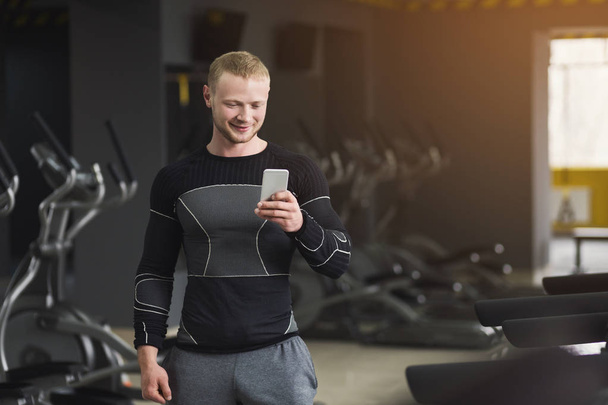 Male bodybuilder using smartphone before workout - Foto, afbeelding