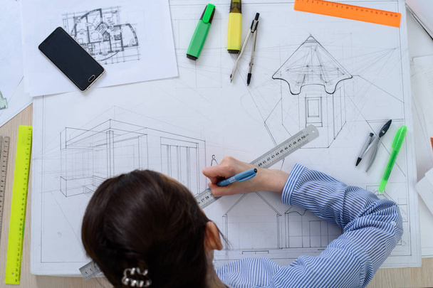 Верхний вид молодого студента, готовящего архитектурные работы за столом с белой чертежной бумагой и канцелярскими принадлежностями
 - Фото, изображение