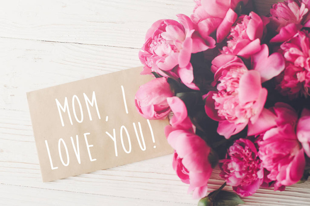 mom, i love you text on craft card and pink peonies bouquet on rustic white wooden background in light. floral greeting card concept, flat lay. happy mother's day . tender image - Photo, Image