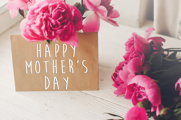 幸せな母の日テキスト クラフト カード、光で素朴な白い木製の窓にピンクのシャクヤク ブーケ。花のグリーティング カードのコンセプトです。母の日。柔らかい柔らかい春の画像 - 写真・画像