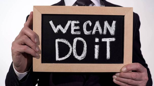 We can do it motivation phrase on blackboard in businessman hands, support - Foto, Bild