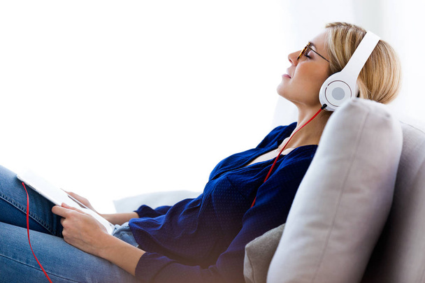 Beautiful young woman listening to music with her digital tablet at home. - 写真・画像