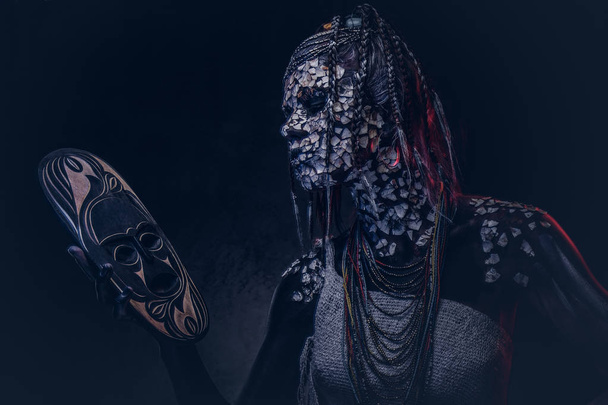 Портрет ведьмы из коренного африканского племени в традиционном костюме. Концепция грима. Изолированный на тёмном фоне
. - Фото, изображение