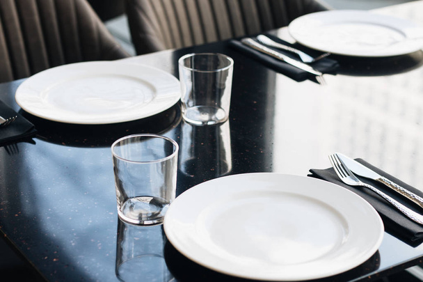 valkoiset lautaset, lasit ja astiat mustalla pöydällä, elegantit pöytäesineet
  - Valokuva, kuva