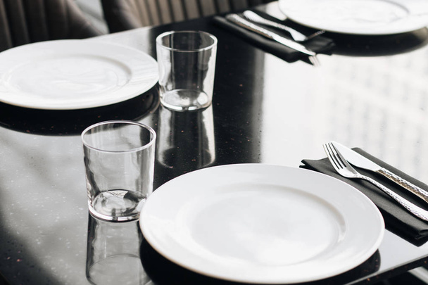 valkoiset lautaset, lasit ja astiat mustalla pöydällä, elegantit pöytäesineet
  - Valokuva, kuva