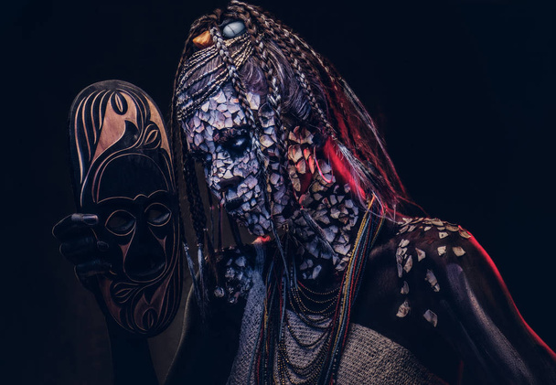 Retrato de cerca de una bruja de la tribu indígena africana, vestida con un traje tradicional. Concepto de maquillaje. Aislado sobre un fondo oscuro
. - Foto, imagen
