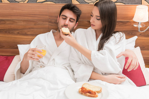 Attractive young couple in white robes, enjoying food and drink  - Foto, afbeelding