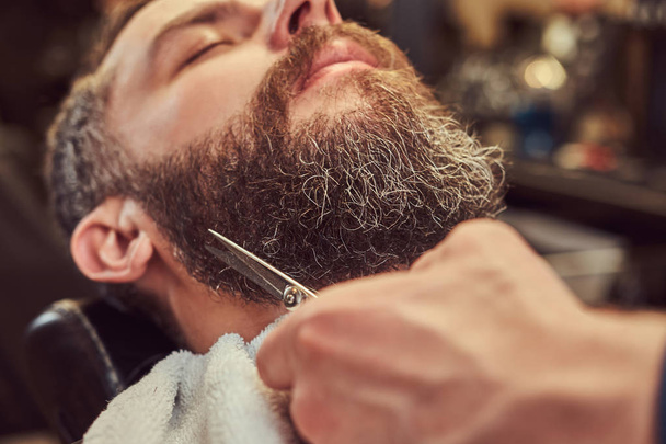 Professional hairdresser modeling beard with scissors and comb at the barbershop. Close-up photo. - Fotó, kép