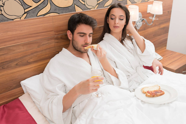 Attractive young couple in white robes, enjoying food and drink  - Foto, imagen